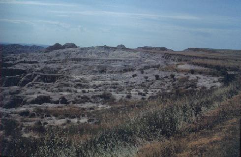 Badlands. Erosion terraces beyond and below top grassy surface. Erosion moves the terraces backward.
